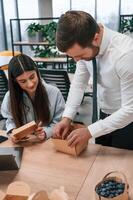 Putting them, on the table. Man and woman are with eco boxes in the office together photo