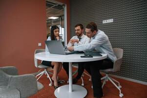 Sitting, talking, using laptop. Office workers are indoors .by the table photo
