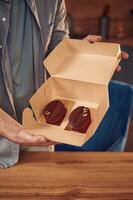 Coffee like look, design of the sweets. Man is with delicious desserts that are in the eco boxes. Standing indoors photo