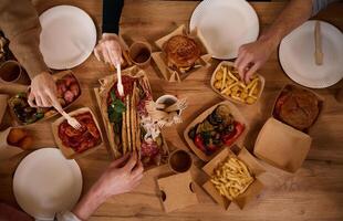 Top view of table with ,food on, it, hands of the people taking it, eating. Meat, vegetables, French fries, burger, mushrooms photo