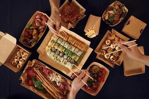 Top, view ,of table with food on it, hands of the people taking it, eating. Meat, sushi, vegetables, French fries, burger, mushrooms photo