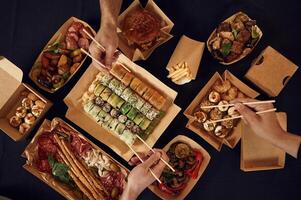 Top view of table with, food ,on it, hands of the people taking it, eating. Meat, sushi, vegetables, French fries, burger, mushrooms photo