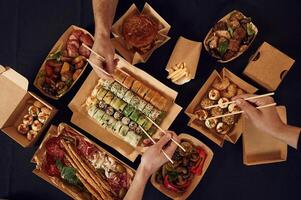 Top view of, table with ,food on it, hands of the people taking it, eating. Meat, sushi, vegetables, French fries, burger, mushrooms photo