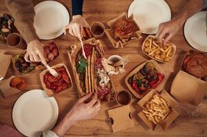 Top view of table with food on it, hands of, the people, taking it, eating. Meat, vegetables, French fries, burger, mushrooms photo