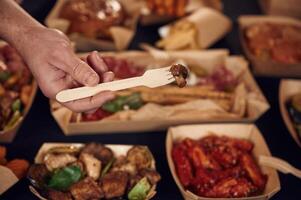 Man is holding ,fork with mushroom. Close up view of table with food on it. Meat, vegetables photo