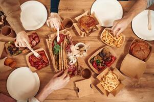 Top view of table with food on it, hands ,of the people taking it, eating. Meat, vegetables, French fries, burger, mushrooms photo