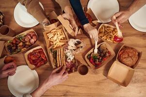 Top view ,of table with food ,on it, hands of the people taking it, eating. Meat, vegetables, French fries, burger, mushrooms photo