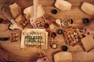Top view of table with ,sushi on it in paper eco boxes, hands of the people taking it, eating photo