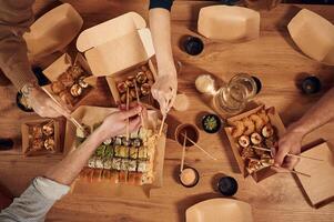 Top view ,of table with sushi on it in paper eco boxes, hands of the people taking it, eating photo