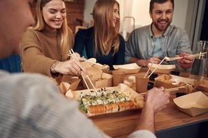 Using ,chopsticks. .Friends are sitting indoors at home and eating sushi together photo