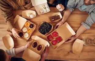 Top view of table with food on ,it, hands of the people taking it, eating. Macarons, blueberries, desserts, pastry meal photo