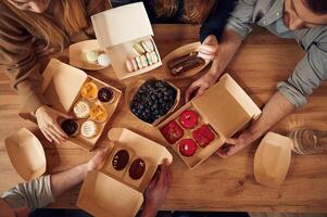 Top, view of table with food on it, hands of the people taking it, eating. Macarons, blueberries, desserts, pastry meal photo