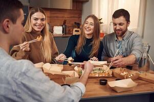 Casual conversation. Friends, are sitting indoors at home and eating sushi together photo
