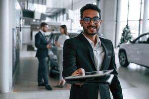 Man ,standing in ,front of his coworkers. Three people are working together in the car showroom photo