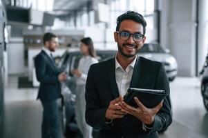 Man standing in ,front ,of his coworkers. Three people are working together in the car showroom photo