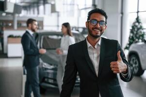 Man standing in, front of his coworkers. Three people are working together in the car showroom photo