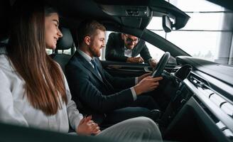 Side view. Car showroom, worker is consulting man ,and woman that are sitting inside of automobile photo
