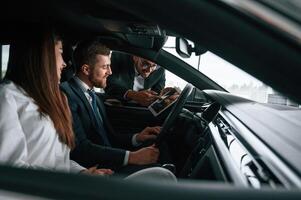Car showroom worker is consulting, man and woman that are sitting inside of automobile photo