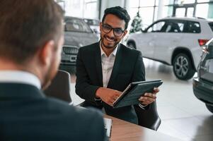 Using ,graphic tablet. Man is consulting the, customer in the car showroom photo