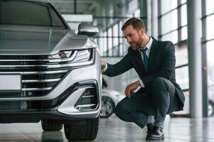 Man in suit and ,tie is sitting and checking quality of the vehicle in the car showroom photo