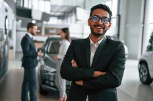 Man standing in front of his coworkers. Three people are working together in the car showroom photo