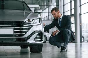 Man in suit and tie is sitting and checking, quality of the vehicle in the car showroom photo