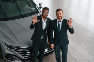Near grey colored automobile. Two businessmen a,re working together in the car showroom photo