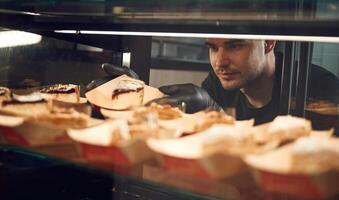 Man is taking delicious desserts by hands that are in black gloves photo