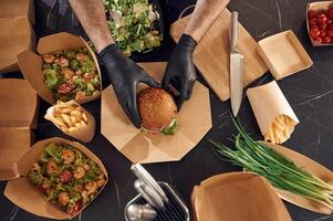 Close up view of, burger, French fries and vegetables. Man is packing food into the paper eco boxes. Indoors, restaurant photo