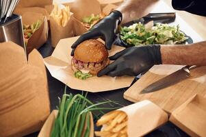 Close ,up view of burger, French fries and vegetables. Man is packing food into the paper eco boxes. Indoors, restaurant photo