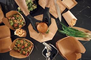 Close up, view of burger, French fries and, vegetables. Man is packing food into the paper eco boxes. Indoors, restaurant photo