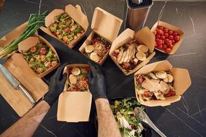 Meat,, vegetables, tomatoes, eggs on the table. Man is packing food into the paper eco boxes. Indoors, restaurant photo