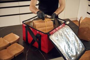 On, the table. Man packs paper eco boxes into a bag for food delivery photo