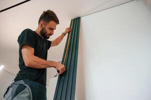 Taking, measurements. Plumber, worker installing heating radiator in empty room of a newly built house photo