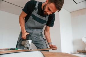 Using, the electric machine tool to cut the plank. Man is installing new laminated wooden floor photo