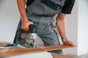 Using the, electric machine tool to cut the plank. Man is installing new laminated wooden floor photo