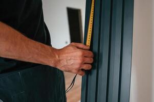 Taking measurements. Plumber worker installing heating radiator in empty room of a newly built house photo