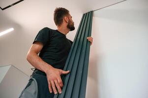Holding tall ,heating radiator. Plumber worker is in empty room of a newly built house photo