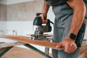 Using, the electric machine tool to, cut the plank. Man is installing new laminated wooden floor photo