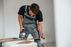Using ,the electric machine tool to cut the plank. Man is installing new laminated wooden floor photo