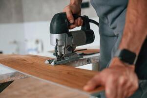 Using the electric machine tool to cut the plank.. Man is installing new laminated wooden floor photo
