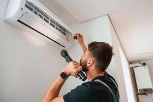 Using ,screwdriver and flashlight. Man repairs an air conditioner indoors at home photo