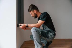 Plumber worker installing heating radiator in empty room of a newly built house photo