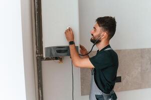 A man, repairs a boiler. Listens to it using a stethoscope photo