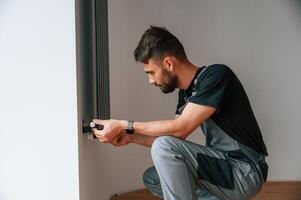 Plumber, worker ,installing heating radiator in empty room of a newly built house photo