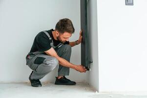 Plumber worker, installing heating radiator in empty room of a newly built house photo