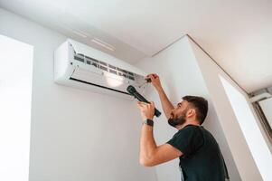 Using screwdriver and, flashlight. Man repairs an air conditioner indoors at home photo