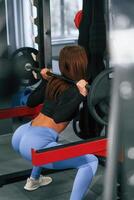 Doing squats with heavy barbell. Beautiful woman with sport body type is in the gym photo