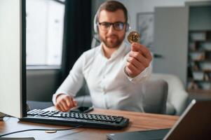 Holding bitcoin, in the hand. Man in formal clothes is working in the modern office. Using computer photo