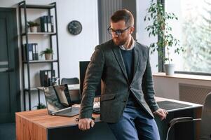 Leaning, on the table. Businessman in suit is in the office with computer photo